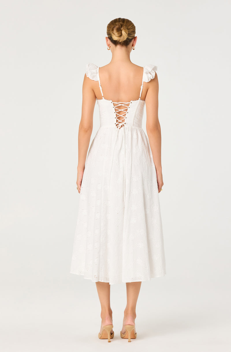 Back view of a woman in a white, eyelet midi dress with puffed shoulder straps and lace-up back.
