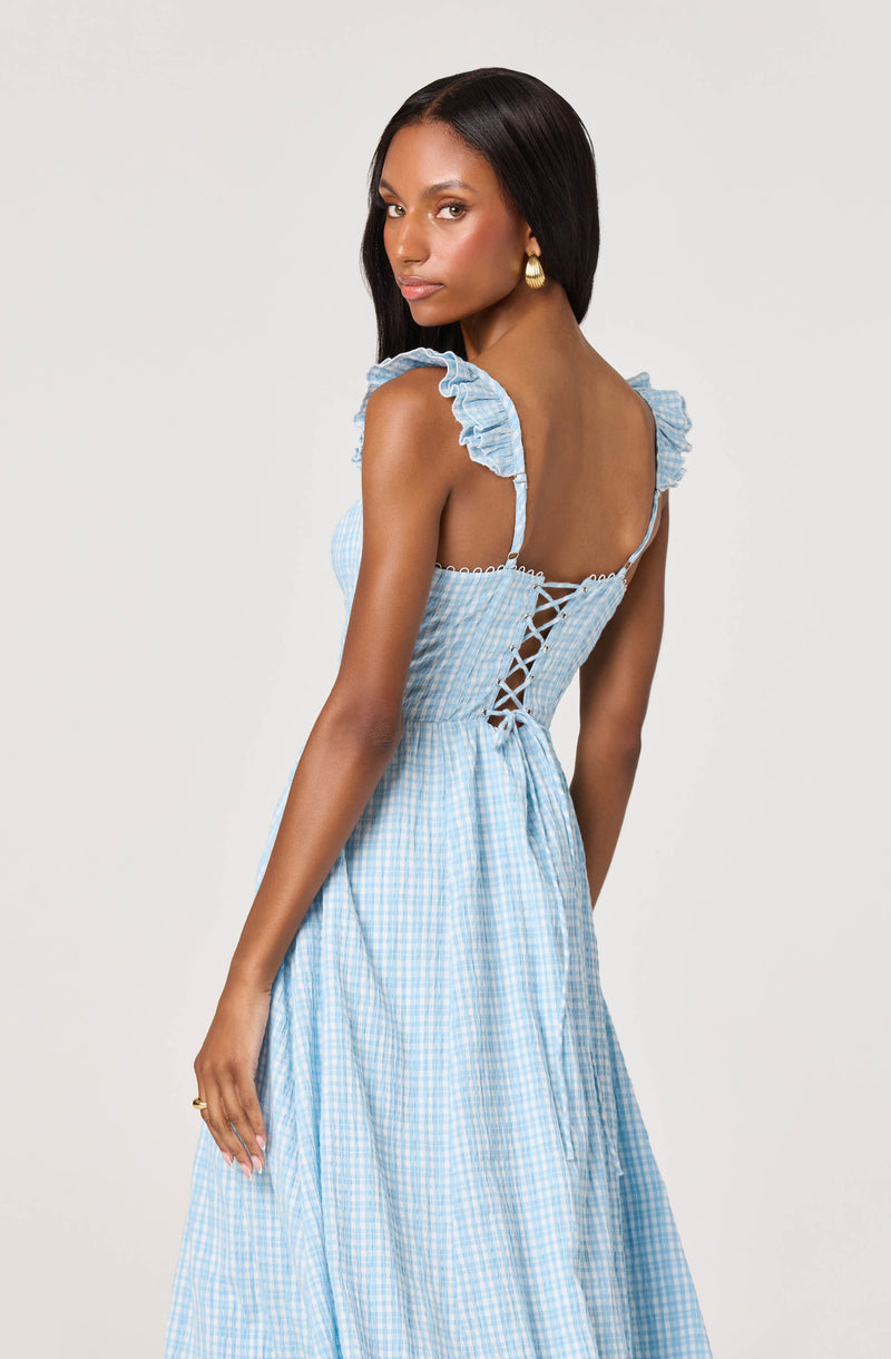 Woman in a blue gingham sundress with ruffled shoulder straps and lace-up back detail.