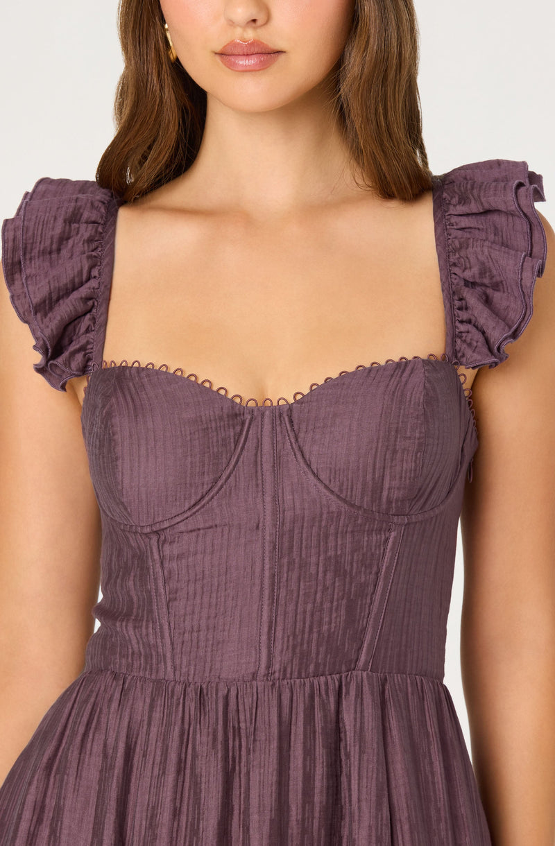 A woman is wearing a mauve-colored dress with a fitted bodice and a gathered skirt. The dress features puffed sleeves made of lightweight, textured fabric with a slightly crinkled appearance and ruffled edges. The bodice has structured seams and a sweetheart neckline with delicate, scalloped trim along the top edge.