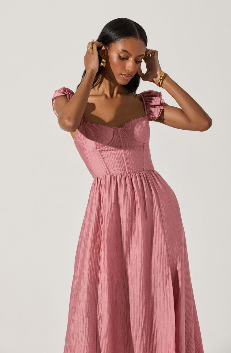 A woman is wearing a pink, textured, pleated maxi dress with puffed short sleeves and a fitted bodice.