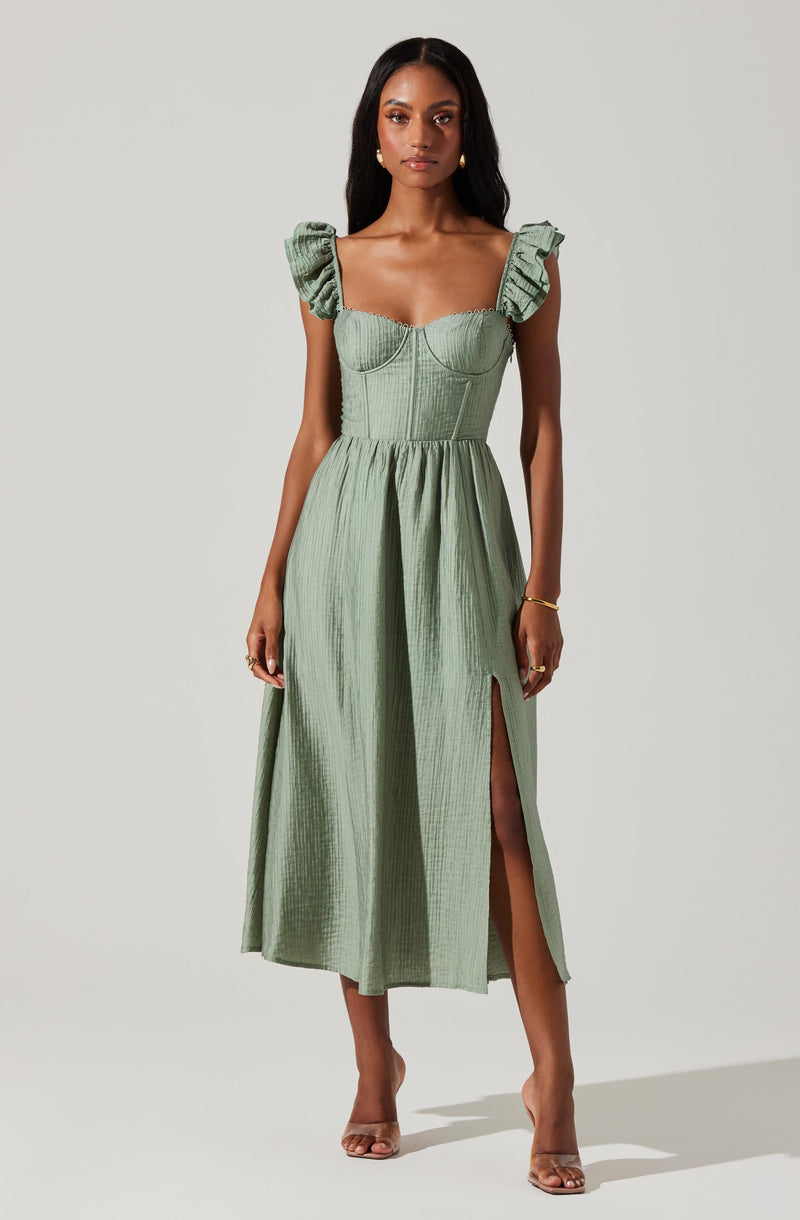 A woman is wearing a light green, textured dress with a fitted bodice and a square neckline. The dress has ruffled shoulder straps and a high waistline, with a long, flowing skirt that features a front slit.