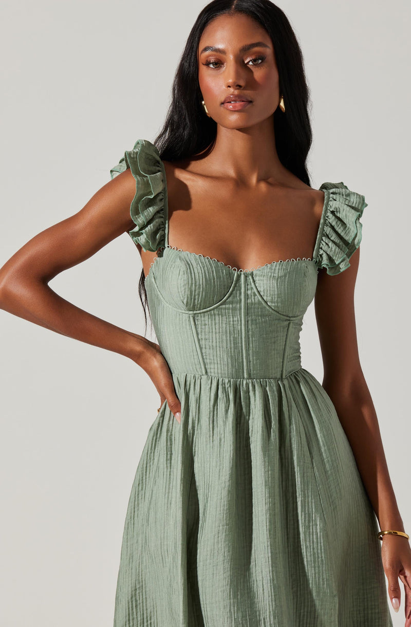 A woman is wearing a light green dress with a fitted bodice and a full skirt. The dress has puffed, ruffled sleeves and a square neckline with boning details. The fabric has a textured, slightly pleated appearance.