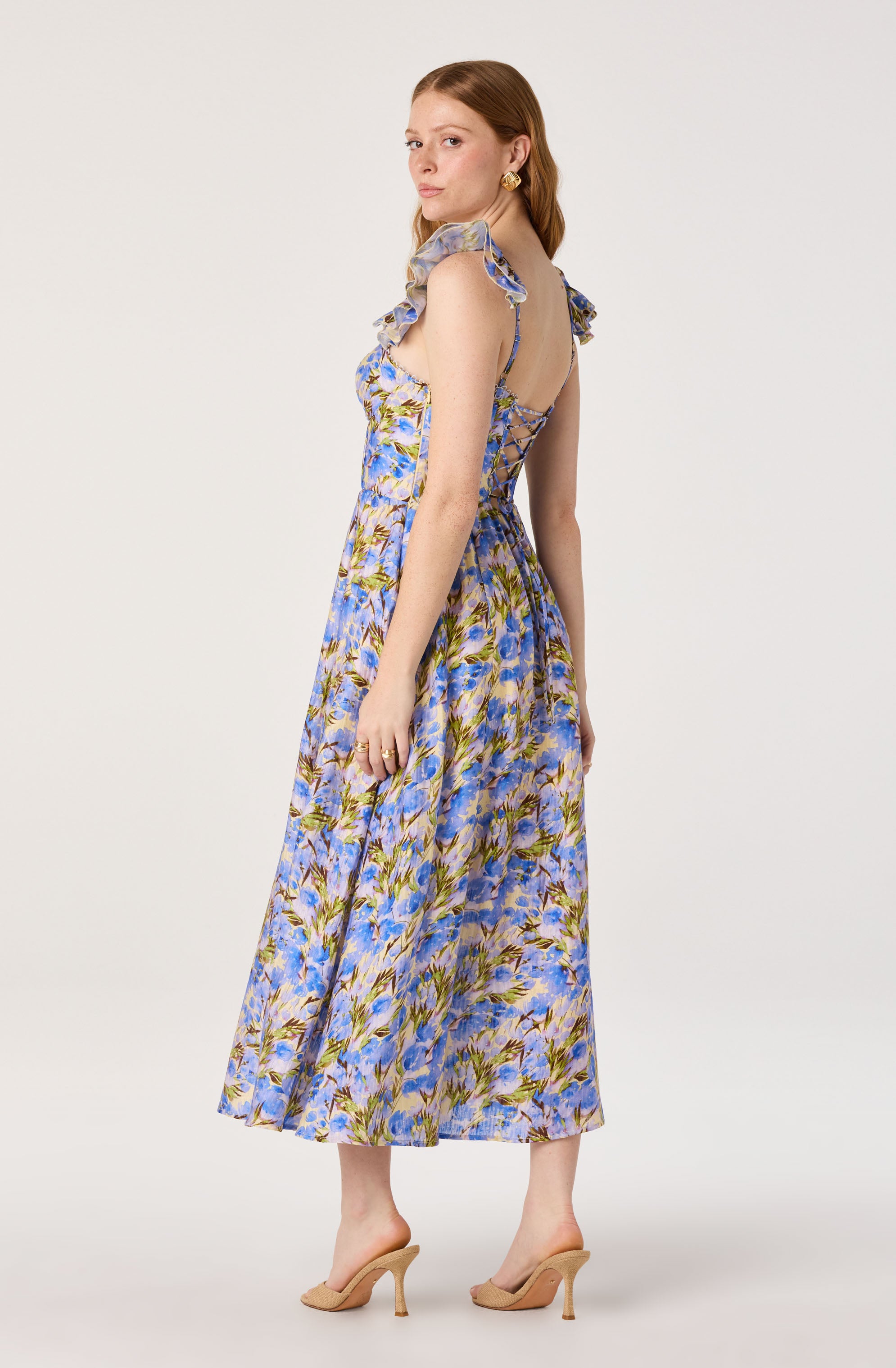 Woman in a floral blue and yellow dress with ruffled shoulder straps and beige heels.