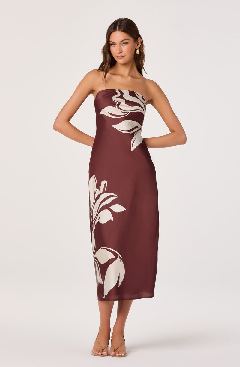 Woman in a strapless maroon dress with large white floral patterns, standing with hands behind her back.