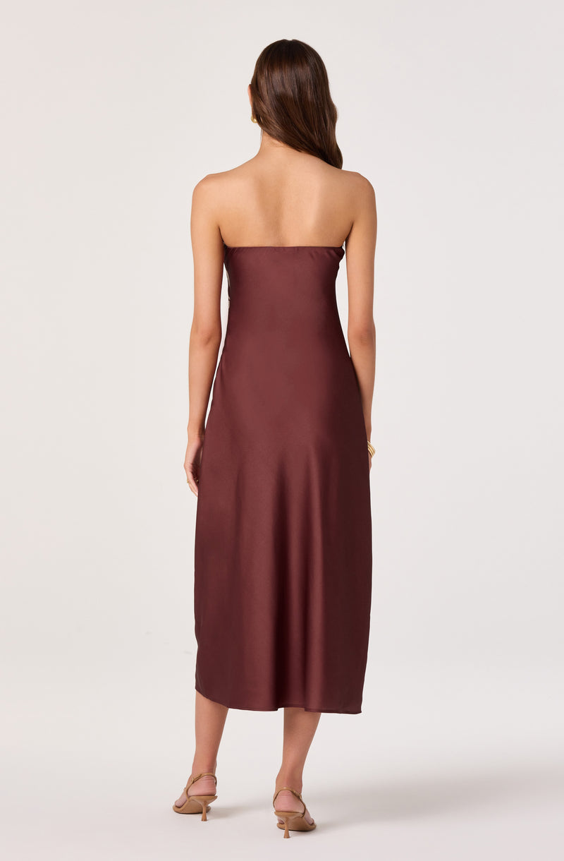 Woman in a strapless, silky, dark red-brown midi dress with beige heels.