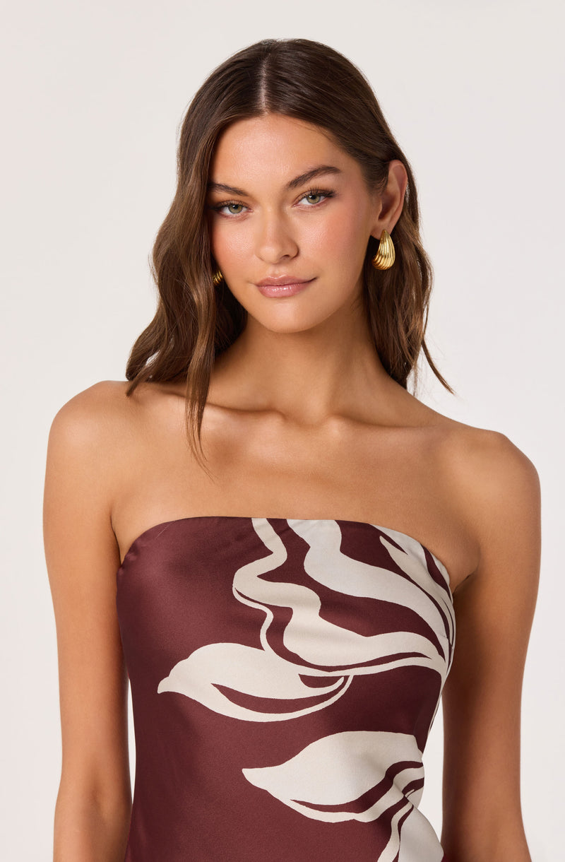 Woman wearing a strapless dress with a brown and white abstract leaf pattern.