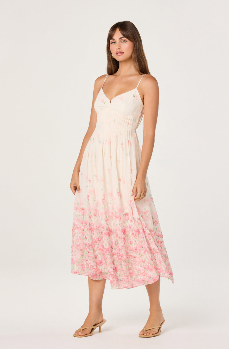 Woman wearing a white, pink, and green floral spaghetti strap sundress with a fitted bodice and flowy skirt.