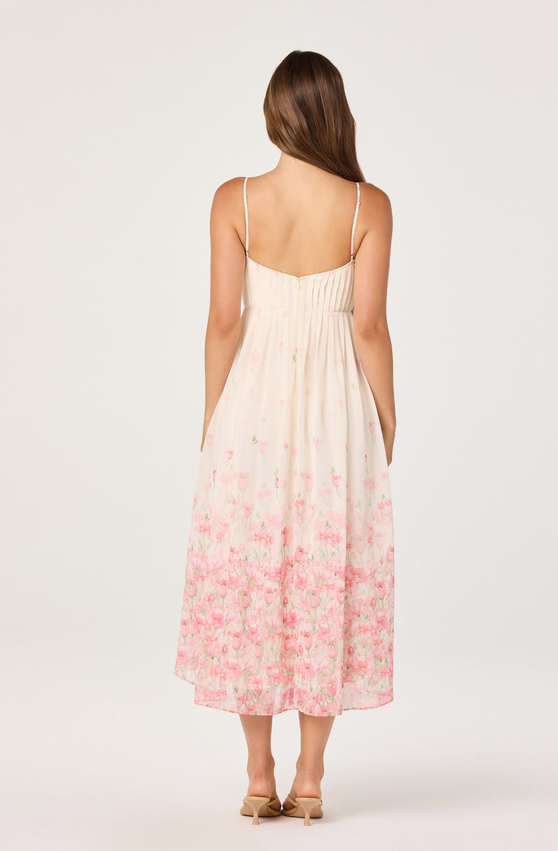 Woman wearing a flowy, sleeveless dress with thin straps, a fitted bodice, and a floral pink pattern at the bottom.