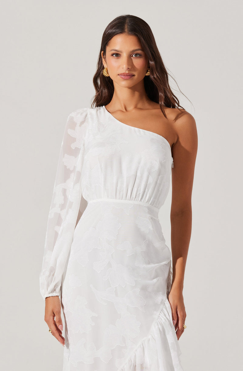 A woman is wearing a white dress with an asymmetrical design featuring one long, sheer, puffed sleeve and a sleeveless off-shoulder section on the other side. The dress has a fitted waist and a textured, floral pattern throughout. She is accessorized with gold earrings.