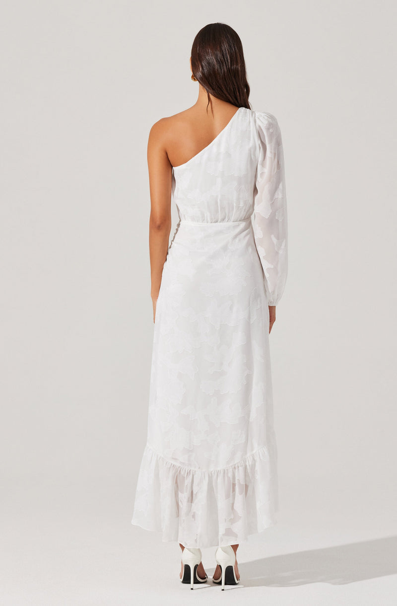 A woman is wearing a long, white, sleeveless dress with a one-shoulder design. The dress features a subtle floral pattern and has a ruffled hemline at the bottom. She is also wearing white high-heeled shoes with black accents.