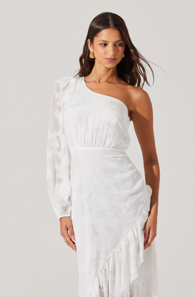 A woman is wearing a white dress with an asymmetrical design. The dress features a one-shoulder style with a long, sheer sleeve on the left side, while the right side is sleeveless. The fabric has a subtle floral pattern and a ruffled hemline that drapes along the bottom.