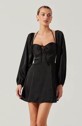 A woman is wearing a black dress with long, puffed sleeves made of shiny satin material. The top of the dress features a ruched bust with a small keyhole opening tied with a bow, and the dress has thin shoulder straps. The skirt is A-line and ends above the knees.