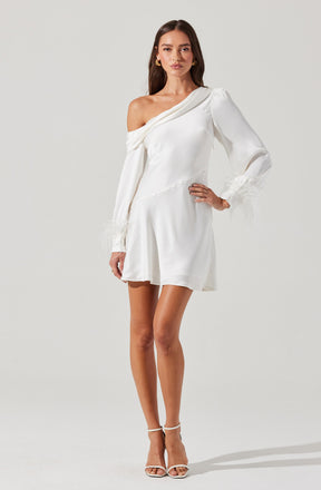 A woman is wearing a white, off-the-shoulder dress with long sleeves. The dress has a draped neckline on one shoulder and sheer, feathered cuffs on the sleeves. The skirt is short and slightly flared. She pairs the dress with white high-heeled sandals.
