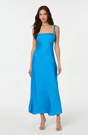 The woman is wearing a long, bright blue satin dress with a straight neckline and thin shoulder straps. She is also wearing strappy high-heeled sandals.