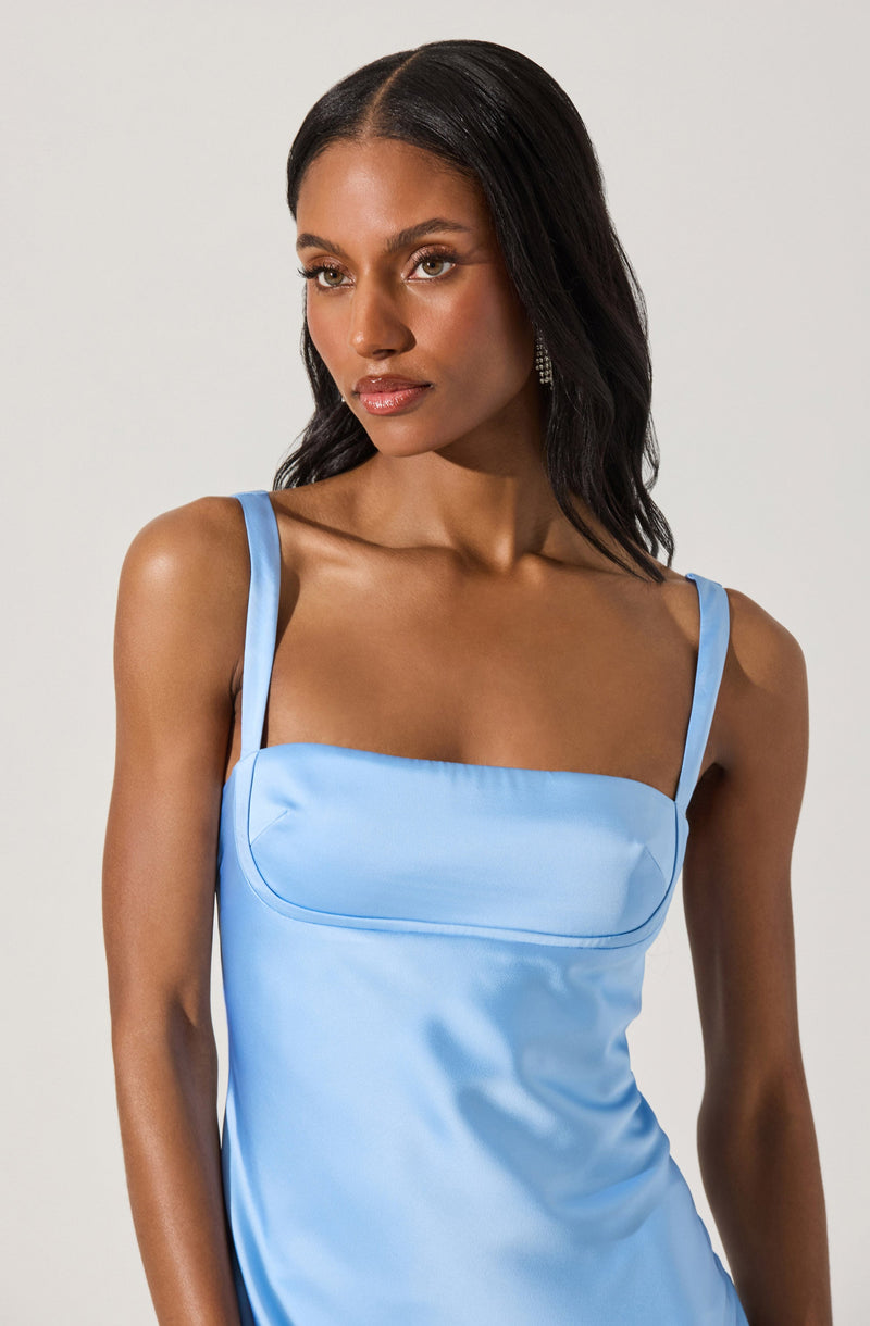 A woman is wearing a light blue satin dress with spaghetti straps. The dress has a fitted bodice with a subtle seam detail across the chest.
