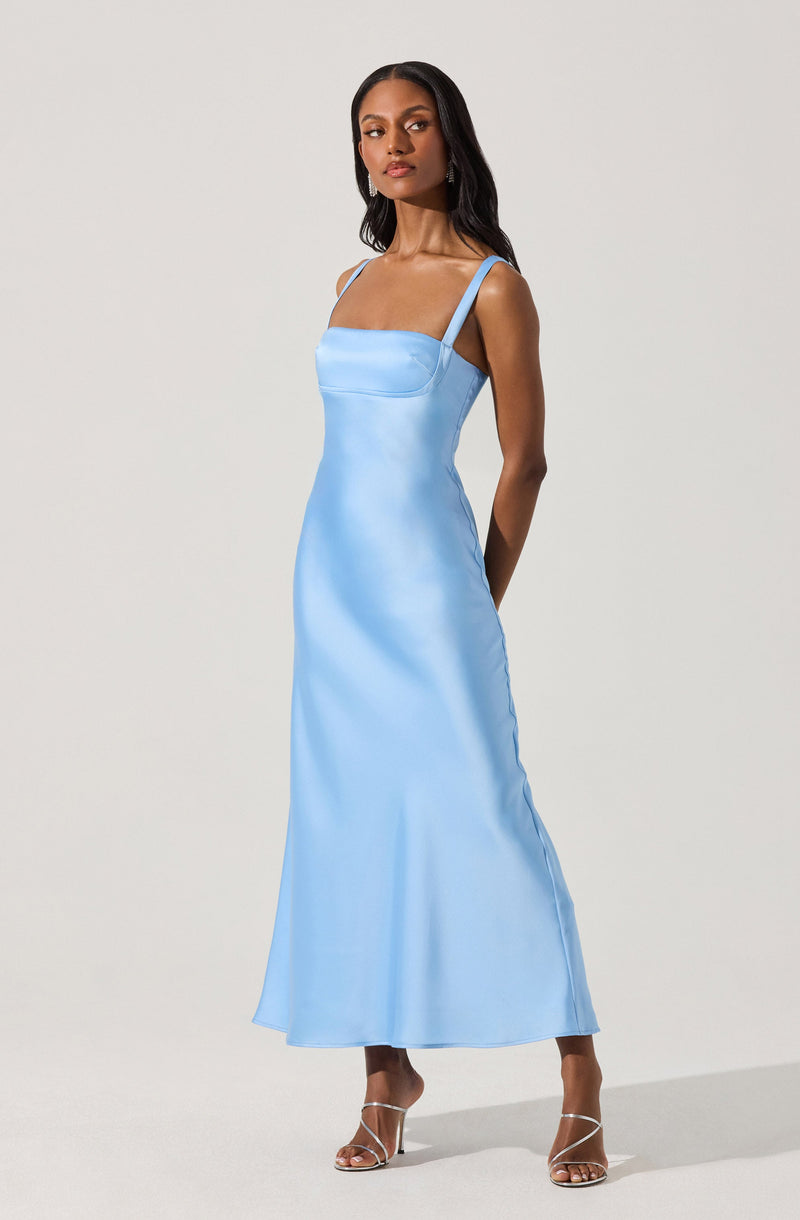 A woman is wearing a light blue satin dress with spaghetti straps and a fitted bodice. The dress extends down to her ankles and has a smooth, shiny texture. She is also wearing open-toe strappy heels.