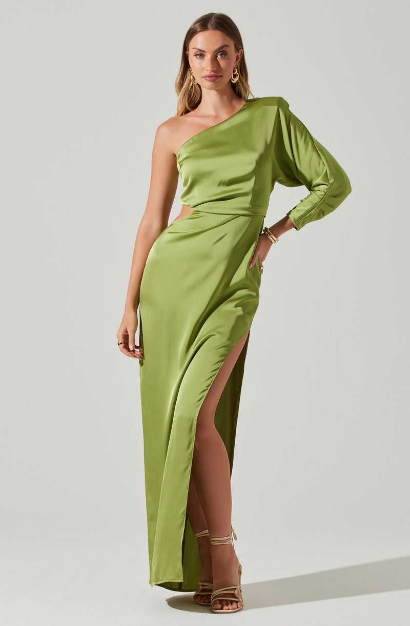 A woman is wearing a shiny, emerald-green satin gown with an asymmetrical, one-shoulder design. The dress features a high slit on the left side, revealing her leg and beige strappy high-heeled sandals. The gown also has a gathered detail around the waist and a puffed long sleeve on her right arm.