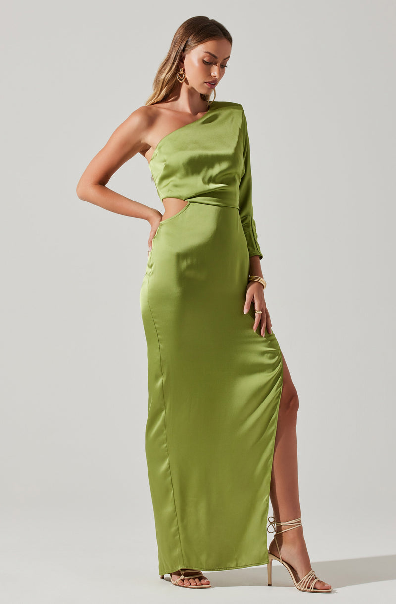 A woman is wearing a floor-length, bright green satin gown with a unique asymmetrical design. The dress features a one-shoulder neckline with a long sleeve on one side, while the other shoulder is bare. There is a cutout on the side of the waist, revealing a hint of skin. The gown has a thigh-high slit on one side, exposing her leg. She is accessorized with large hoop earrings, bracelets, and strappy high-heeled sandals.