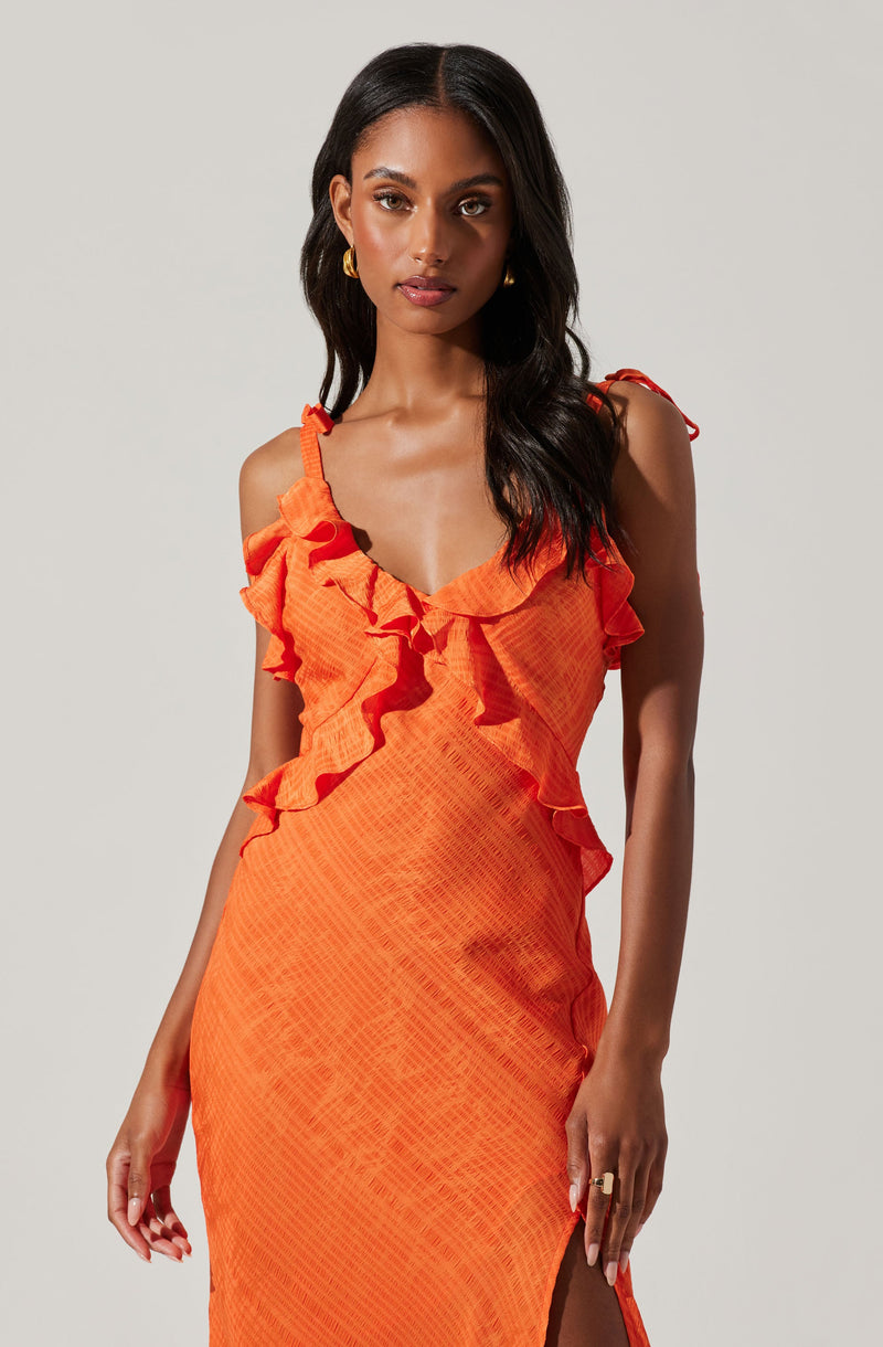A woman is wearing a sleeveless, bright orange dress with ruffled straps and a ruffle detail along the neckline. The dress has a textured, slightly crinkled fabric and a side slit.