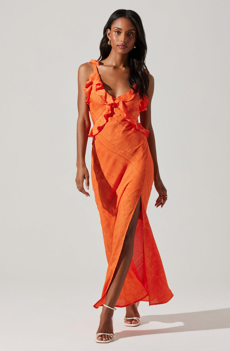 A woman is wearing an orange sleeveless maxi dress with ruffled straps and detailing around the neckline. The dress has a slit up the front, revealing her legs and high-heeled sandals. The fabric appears lightweight with a textured pattern.