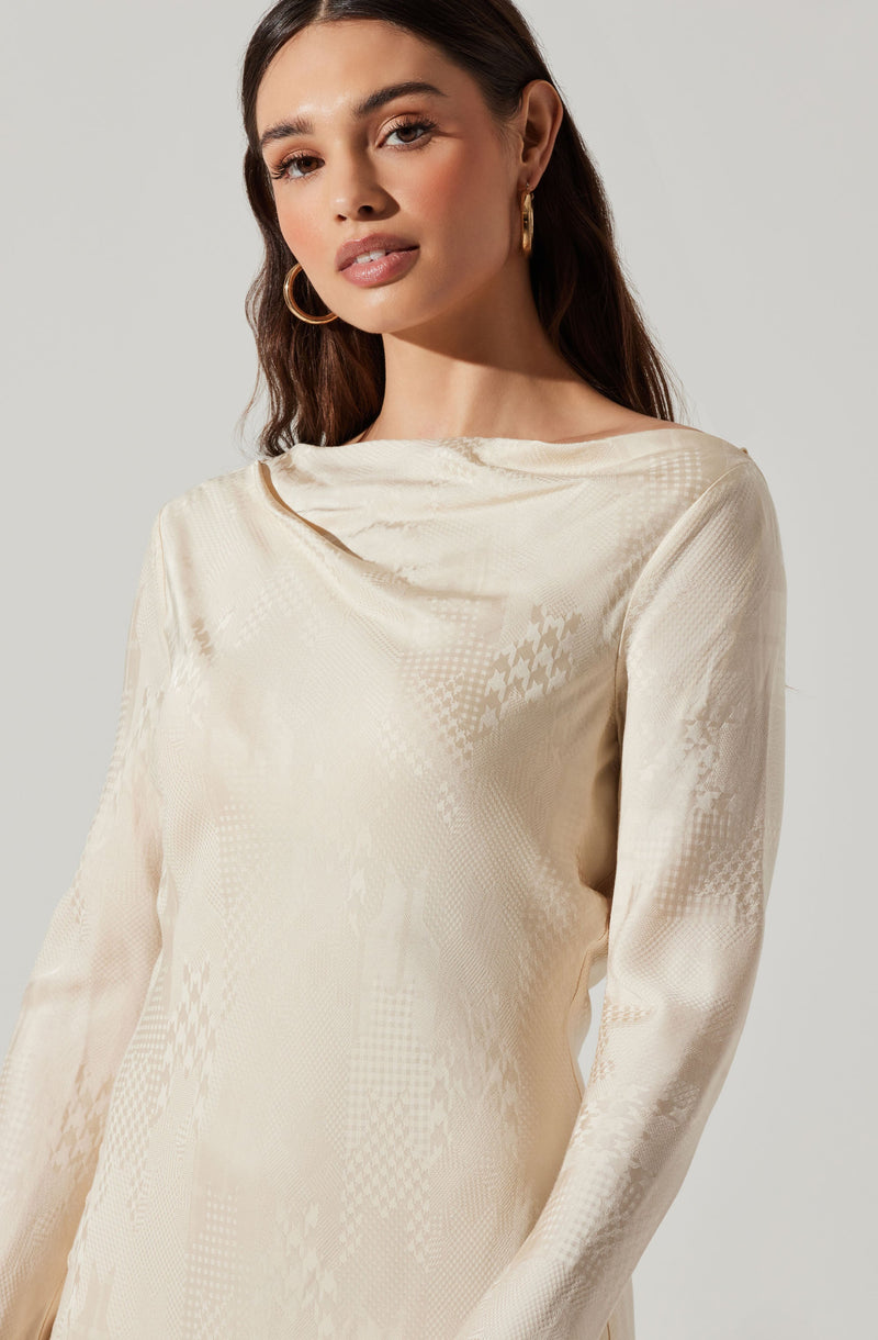 A woman is wearing an elegant, long-sleeved, cream-colored dress made of a shiny, satin-like fabric. The dress features a subtle, intricate pattern with a textured, jacquard appearance.
