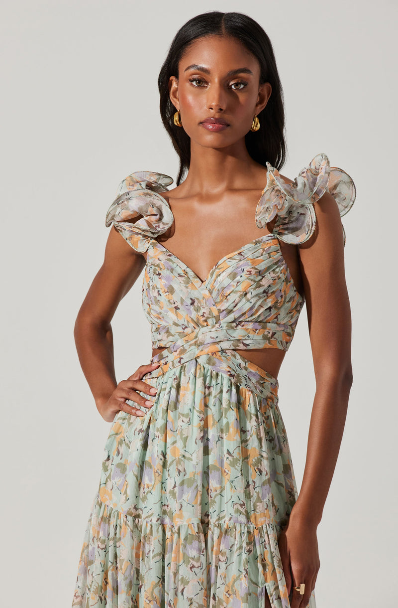A woman is wearing a matching two-piece outfit with a floral print. The top is a cropped blouse with puffed, ruffled shoulders and a sweetheart neckline, with pleated fabric that wraps around her torso. The skirt is high-waisted, flowing, and gathered with a tiered hem, featuring the same floral pattern as the top. She is accessorized with gold hoop earrings.