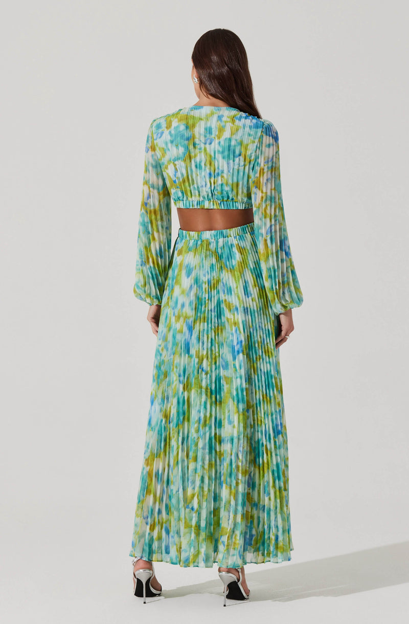 A woman is wearing a matching two-piece outfit with a colorful abstract pattern in shades of blue, green, and yellow. The top is a long-sleeved, cropped blouse with puffed sleeves, and the skirt is a high-waisted, full-length pleated skirt. The fabric appears lightweight and flowy, with a slightly sheer quality.