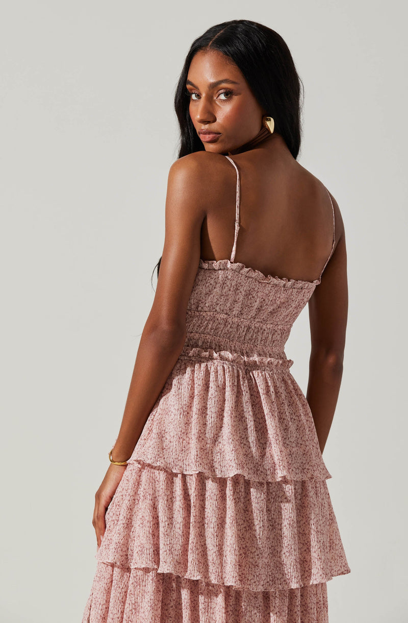 A woman is wearing a sleeveless, pink, tiered dress with thin spaghetti straps. The dress features a smocked bodice and multiple ruffled layers in the skirt.