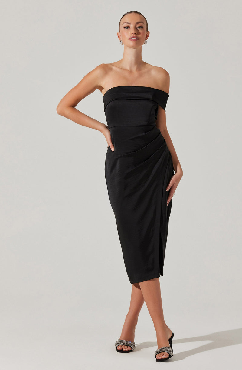 A woman is wearing a strapless black dress that is fitted and has a textured, slightly shiny fabric. The dress features a straight neckline across the chest, with a relaxed, ruched detail on the side. She is also wearing open-toed high heels with embellishments on the straps.
