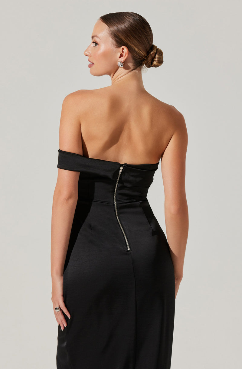A woman is wearing a strapless black dress with an off-the-shoulder style sleeve on one arm, secured with a visible silver zipper running down the back. The dress appears to be made of a shiny, satin-like material that drapes smoothly over her body.