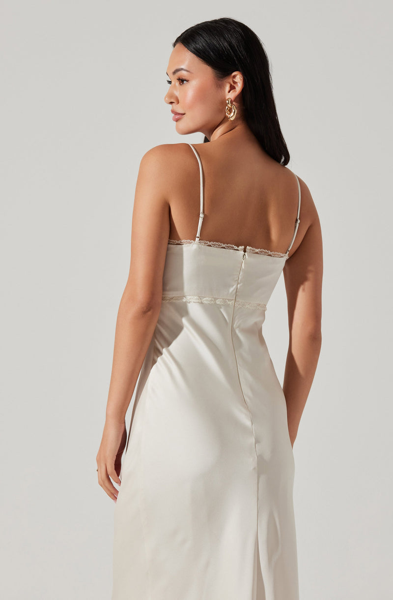 A woman is wearing a sleeveless, satin-like dress with thin spaghetti straps. The dress has lace trim along the upper edge and a fitted waistline. The fabric appears smooth and shiny, giving it an elegant look.