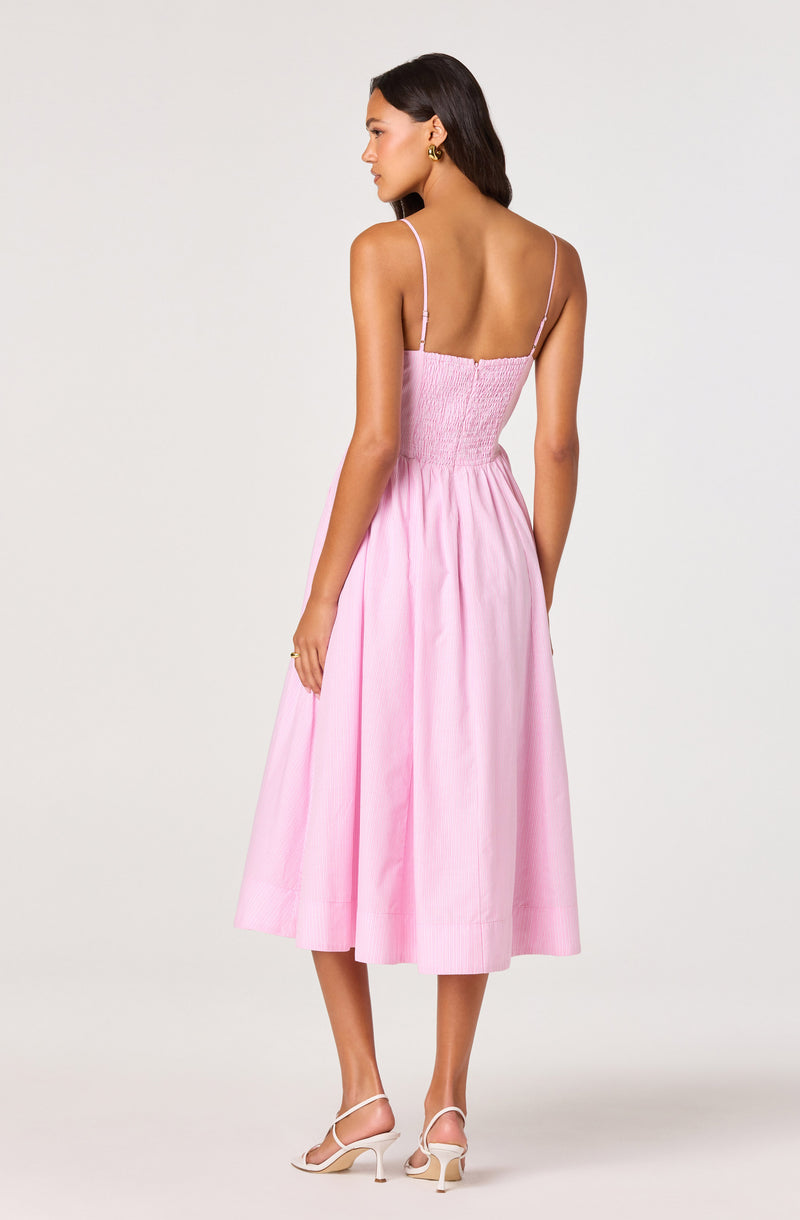 Woman in pink sleeveless, midi-length dress with thin straps and high-waisted, gathered skirt.