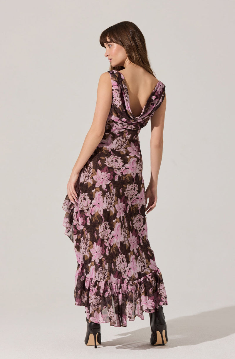 A woman is wearing a sleeveless, floor-length dress with a floral pattern featuring large pink and brown flowers. The dress has a deep cowl neckline and a ruffled hem at the bottom.