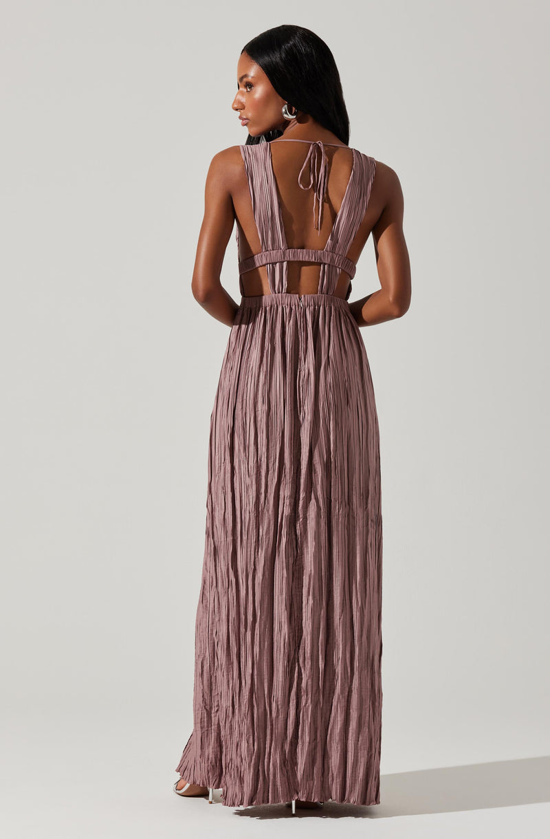 A woman is wearing a sleeveless, floor-length dress with a pleated, metallic mauve fabric. The dress features a back design with cutouts at the waist and an open back with a tie at the upper back. The fabric has a shiny, textured appearance with vertical pleats.