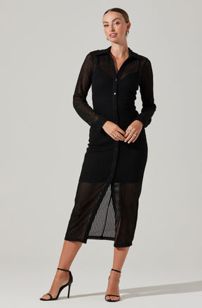 A woman is wearing a black, long-sleeved button-up dress made of a see-through, mesh fabric with a striped pattern. The dress has a collar and a front slit that reveals her legs. She is also wearing black high-heeled sandals with ankle straps.