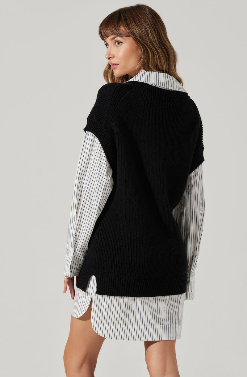 A woman is wearing a black sleeveless knit vest over a long-sleeved button-up shirt with vertical black and white stripes. The shirt's hem extends below the vest, and the shirt's cuffs are visible at the wrists.