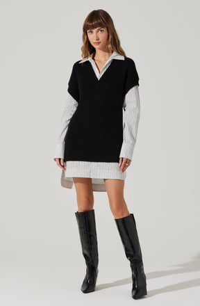 A woman is wearing a white shirt with thin black vertical stripes beneath a black sleeveless knit sweater vest. The shirt extends below the vest, creating a layered look, and the hem of the shirt is slightly longer in the back. She is also wearing a short, matching striped skirt and knee-high black patent leather boots.