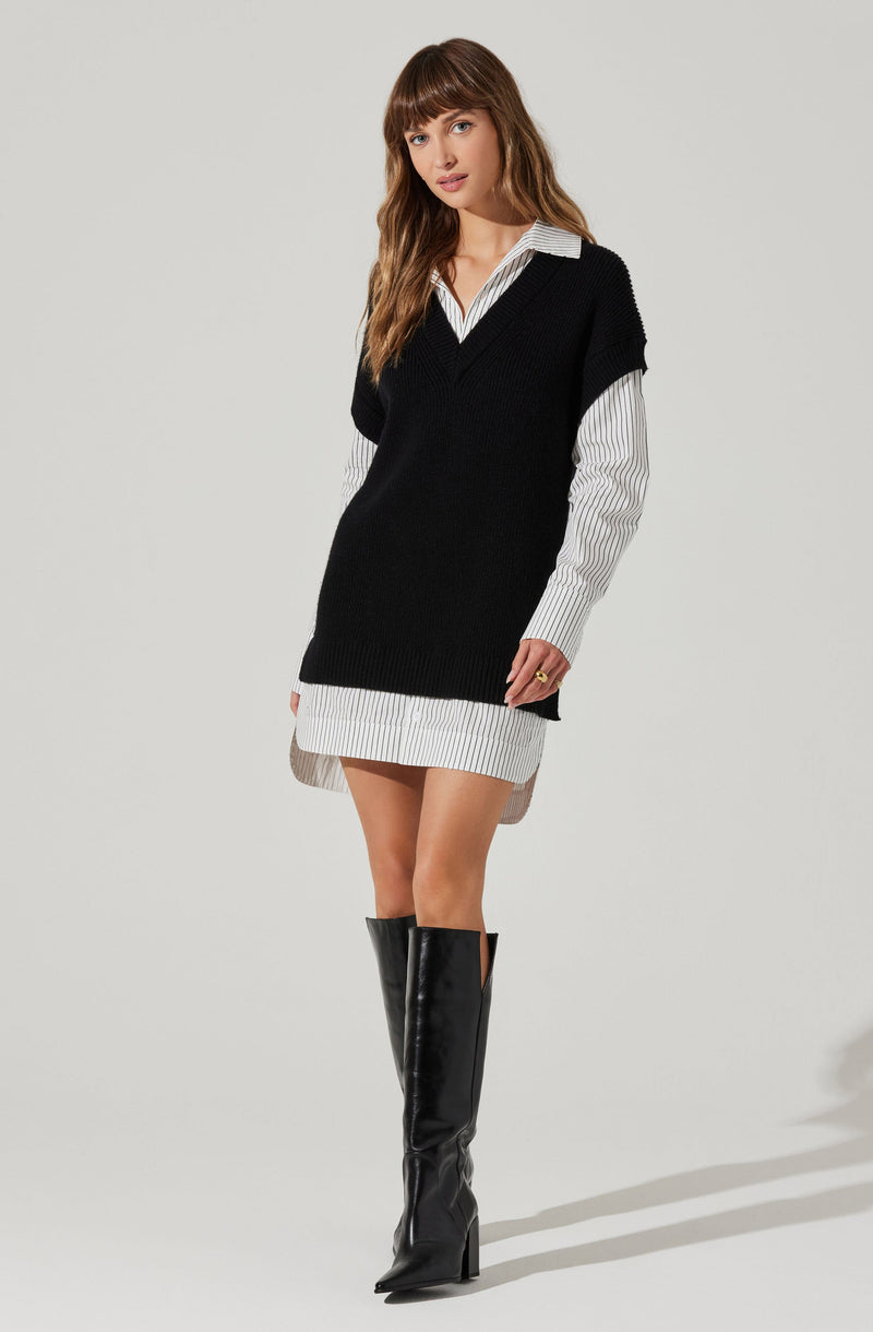 A woman is wearing a white and gray vertically striped shirt with a collar, layered under a sleeveless black V-neck sweater vest. She has on a short, gray, striped mini skirt that matches the shirt. She is also wearing tall, black, shiny knee-high boots with high heels.