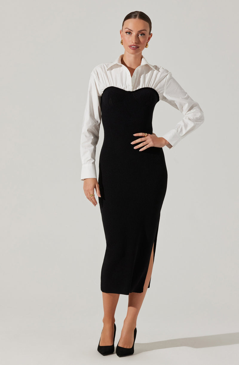 A woman is wearing a white long-sleeved button-up shirt underneath a black, strapless, ribbed knit dress that extends to mid-calf. The dress features a high slit on one side. She is also wearing black high-heeled shoes and gold jewelry, including earrings and rings.