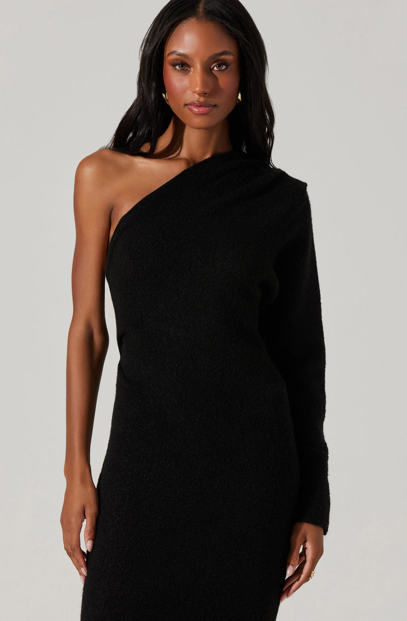 A woman is wearing a black, one-shoulder dress with a textured, knit-like fabric. The dress covers her body from the chest down, with one sleeve that drapes over her right shoulder, leaving her left shoulder exposed.