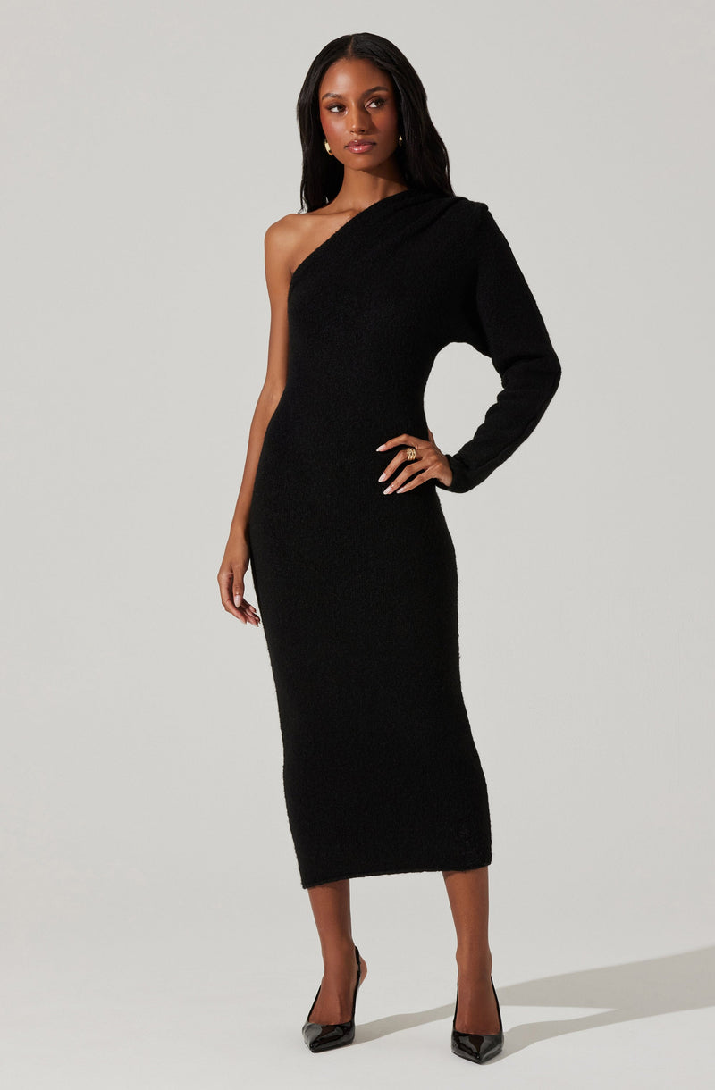 A woman is wearing a black, one-shoulder, long-sleeve knit dress that fits snugly and extends to mid-calf. She pairs the dress with black pointed-toe high heels and gold earrings.