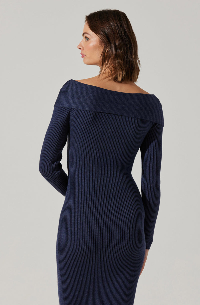 A woman is wearing a fitted, ribbed knit dress in a dark navy blue color. The dress features a wide, off-the-shoulder neckline that sits around her shoulders, and the long sleeves extend to her wrists. The ribbed texture runs vertically throughout the dress.
