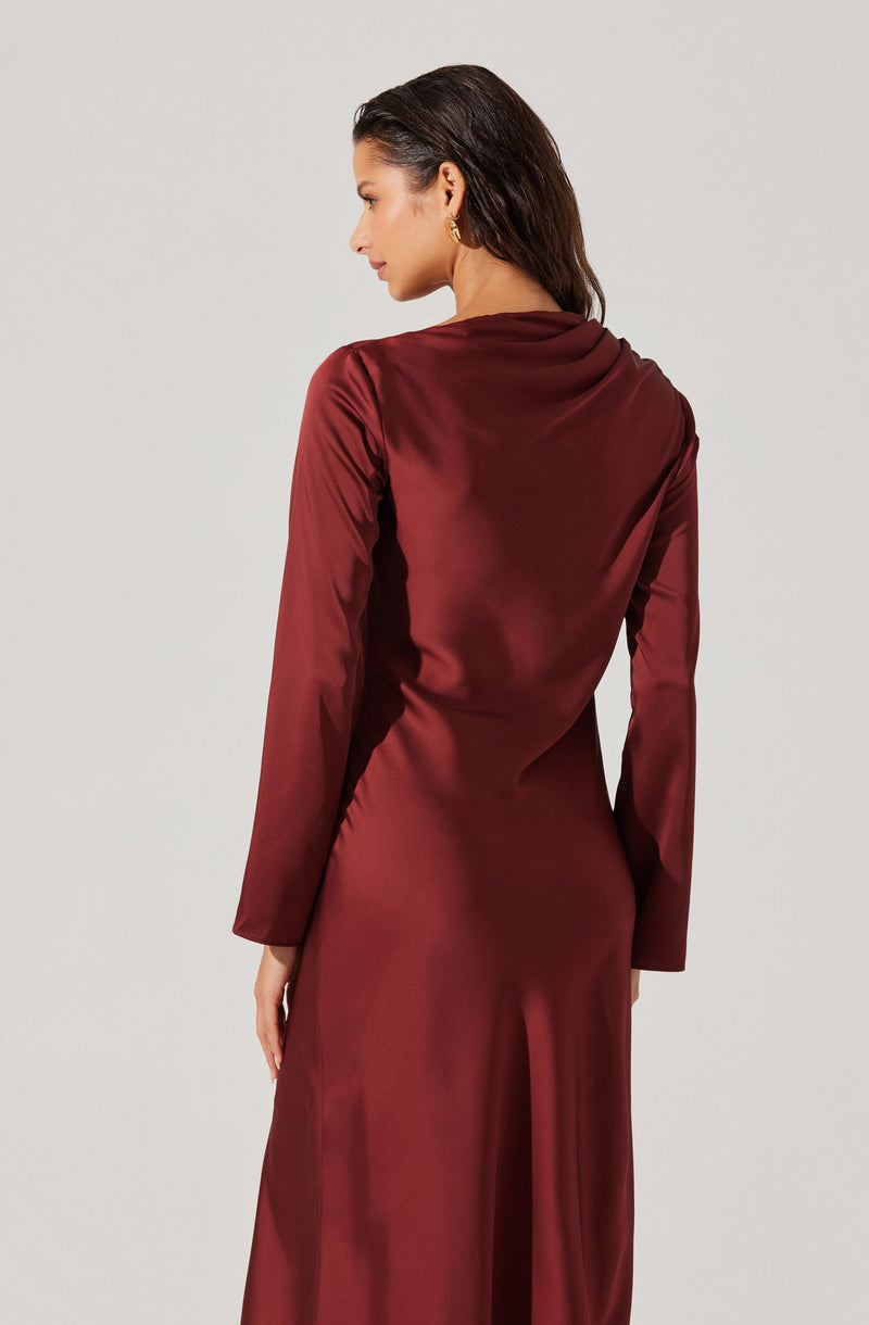 A woman is wearing a long, elegant, burgundy satin dress with long sleeves. The dress has a smooth, shiny finish and a fitted silhouette that drapes gently over her body. The fabric appears luxurious and soft, with a subtle sheen that catches the light.