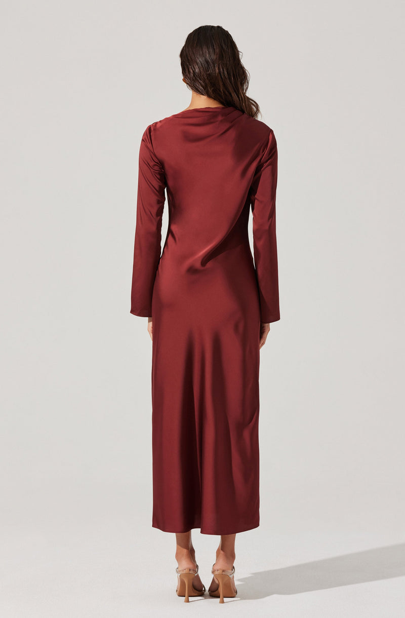 A woman is wearing a long, elegant, burgundy satin dress with long sleeves. The dress has a smooth, shiny texture and reaches down to her ankles. She is also wearing tan high-heeled shoes.