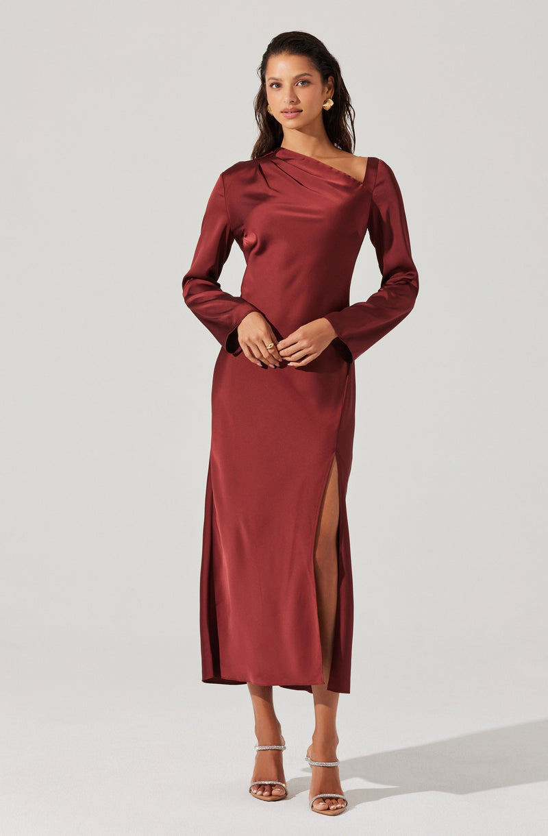 The woman is wearing a long, satin burgundy dress. The dress features a boat neckline with a draped design across the chest, long sleeves, and a high slit on one side revealing her leg.