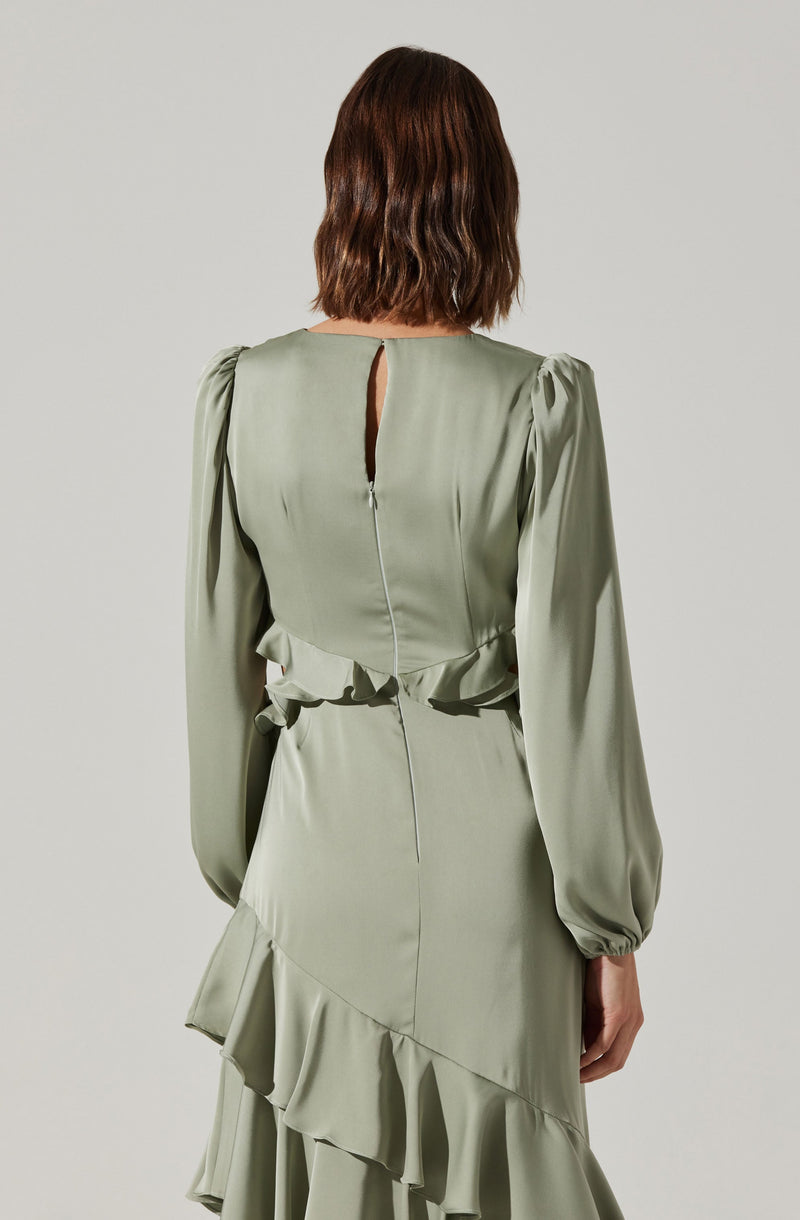 A woman is wearing a light green dress made of a shiny, satin-like fabric. The dress features long, puffed sleeves with elastic cuffs, a small keyhole opening at the back neckline, and a visible silver zipper running down the center back. The skirt of the dress has layered ruffles, creating a flowing and textured silhouette.