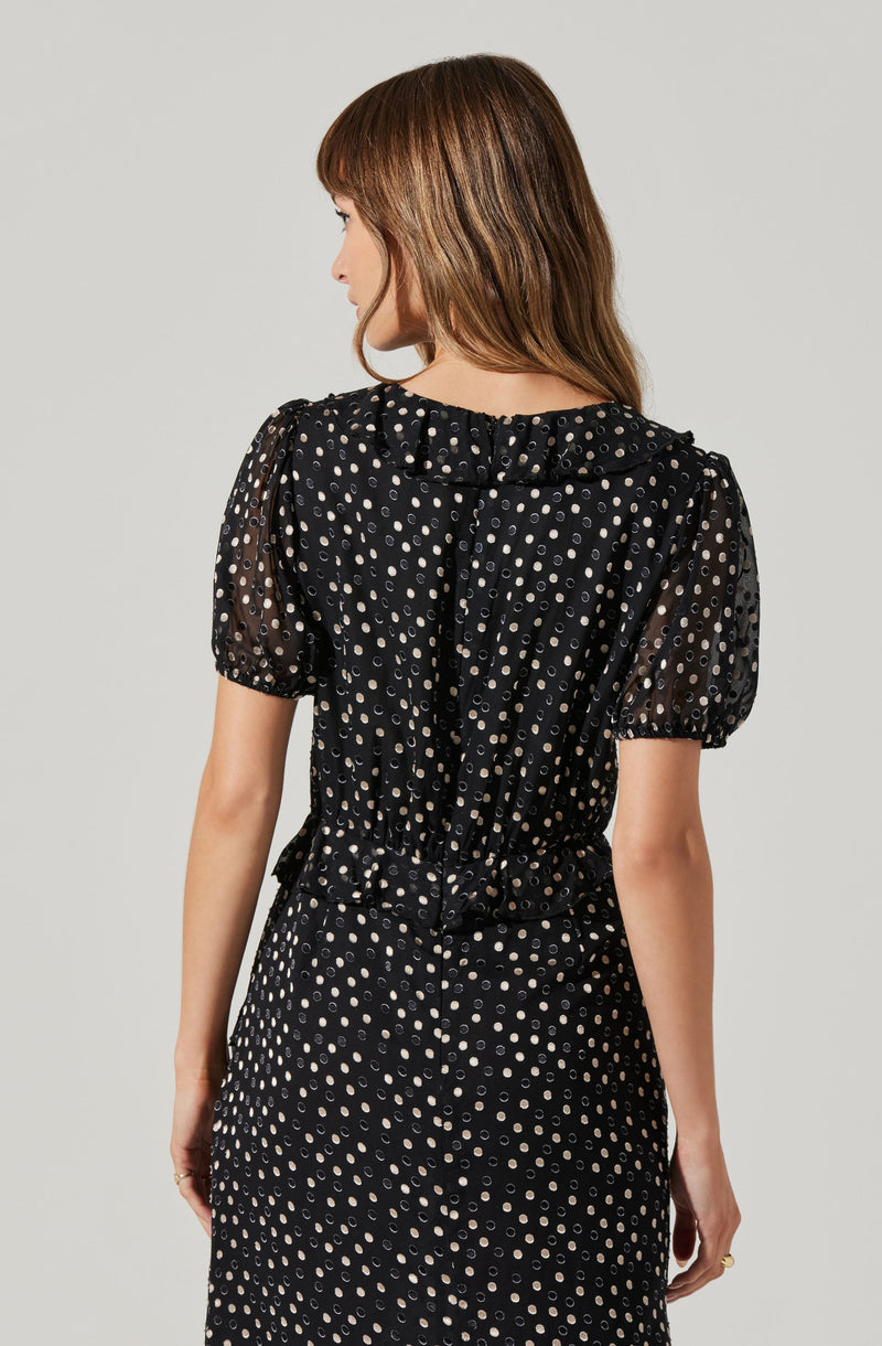 A woman is wearing a black dress with a pattern of small, light-colored polka dots. The dress has short, puffed sleeves and a ruffled collar.