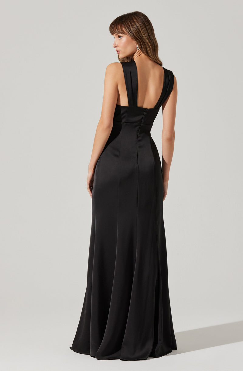 A woman is wearing a long, black satin evening gown with wide shoulder straps. The gown features a fitted bodice and a floor-length skirt that flows elegantly to the ground. The back of the dress has a deep V-cut, exposing her upper back.
