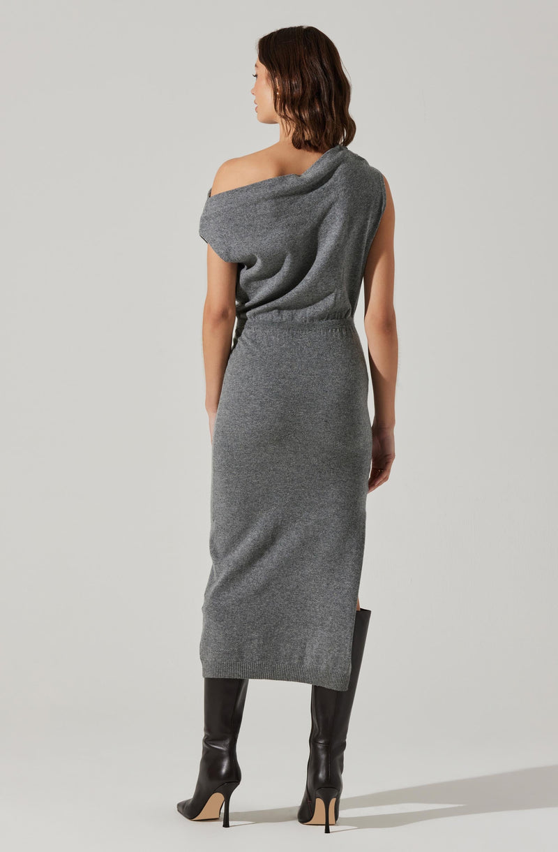 A woman is wearing a gray, sleeveless, knitted dress with an off-the-shoulder style. The dress is fitted at the waist and reaches below the knees. She is also wearing tall black high-heeled boots.
