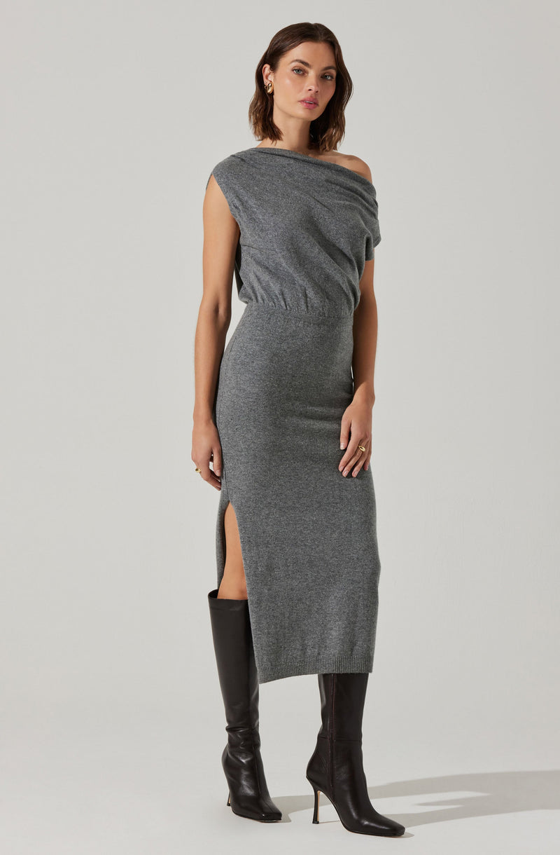A woman is wearing a gray, one-shoulder, midi-length dress with a side slit. The dress appears to be made of a soft, knit fabric that fits snugly around her body. She pairs the dress with tall black heeled boots.